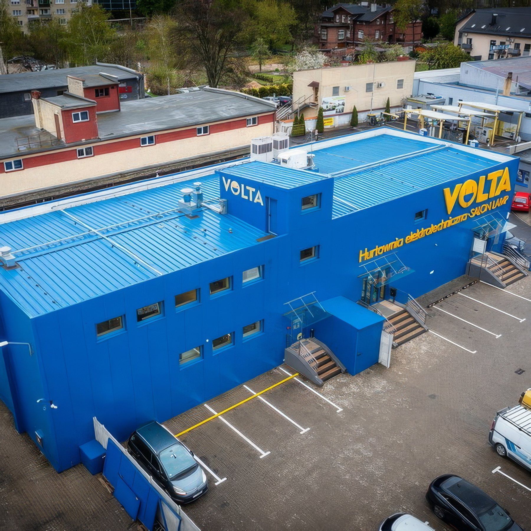 Widok z drona na niebieski budynek hurtowni elektrotechnicznej Volta z parkingiem